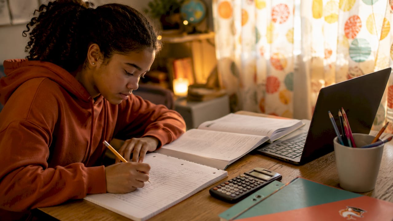 Teen girl doing math homework with laptop nearby
