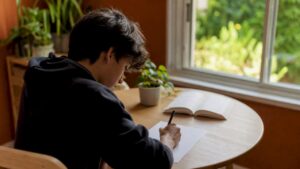 Un adolescent concentré rédige une rédaction assis à son bureau.